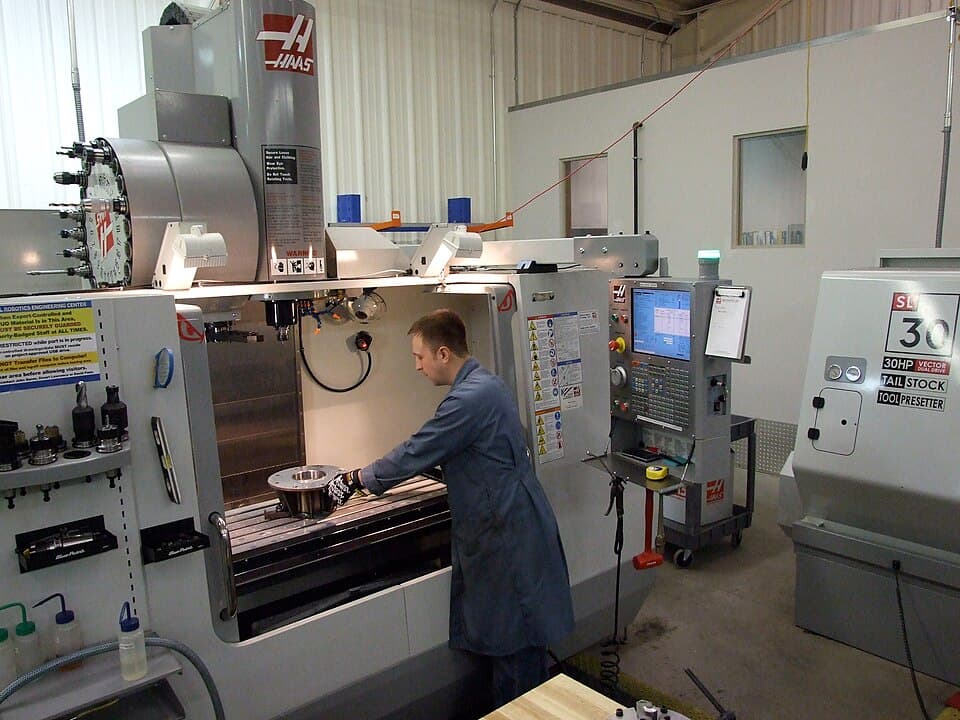 Photo of a small business production or shop floor from a walkthrough perspective: machinery of visible age, work in progress staged on the floor, staff working. Should read as an operating business being inspected, not a staged stock photo of a boardroom handshake.